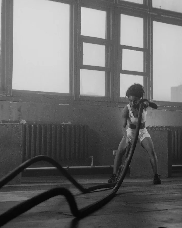 A woman training with battle ropes in a gym, in black and white.