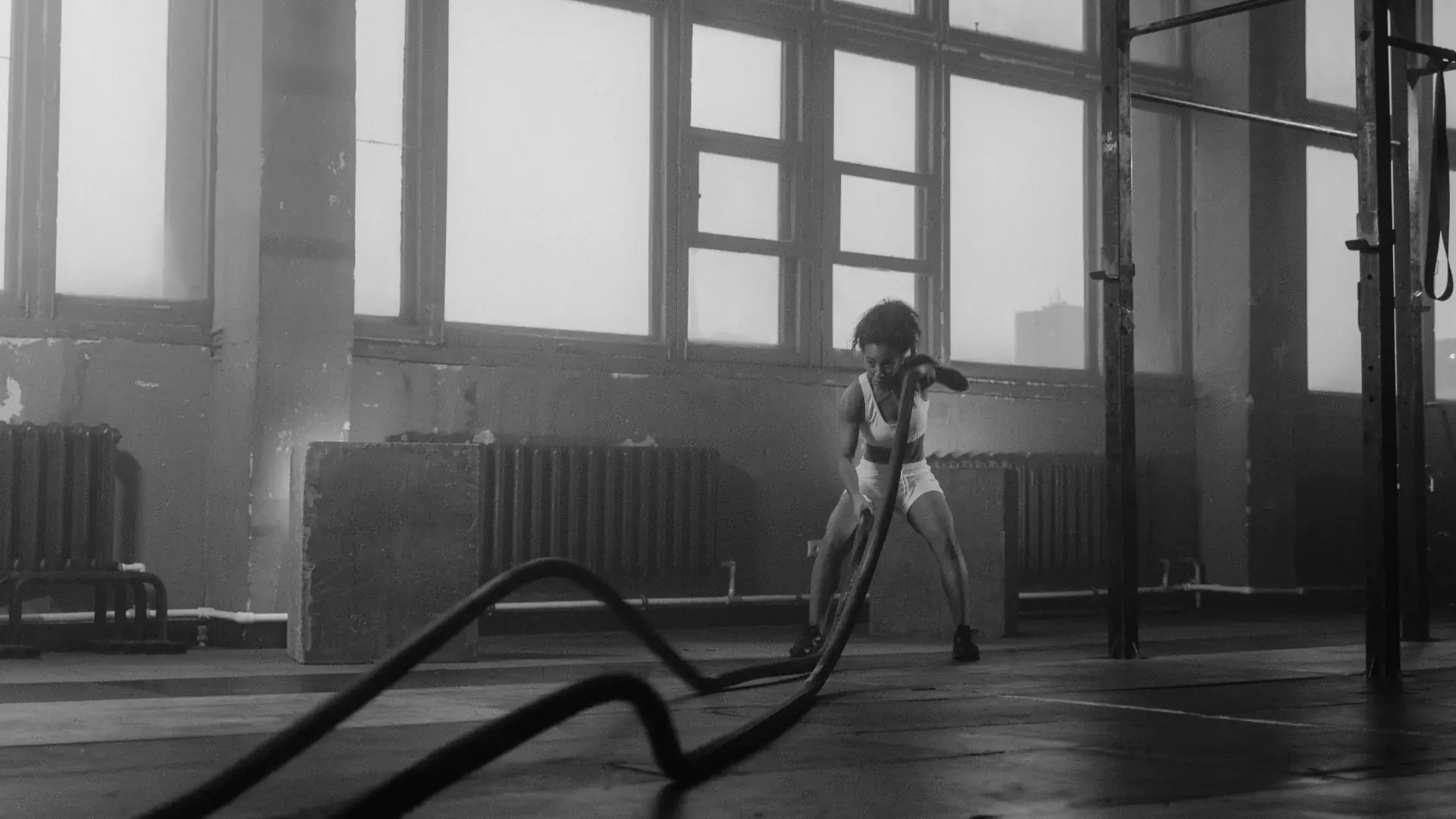 A woman training with battle ropes in a gym, in black and white.