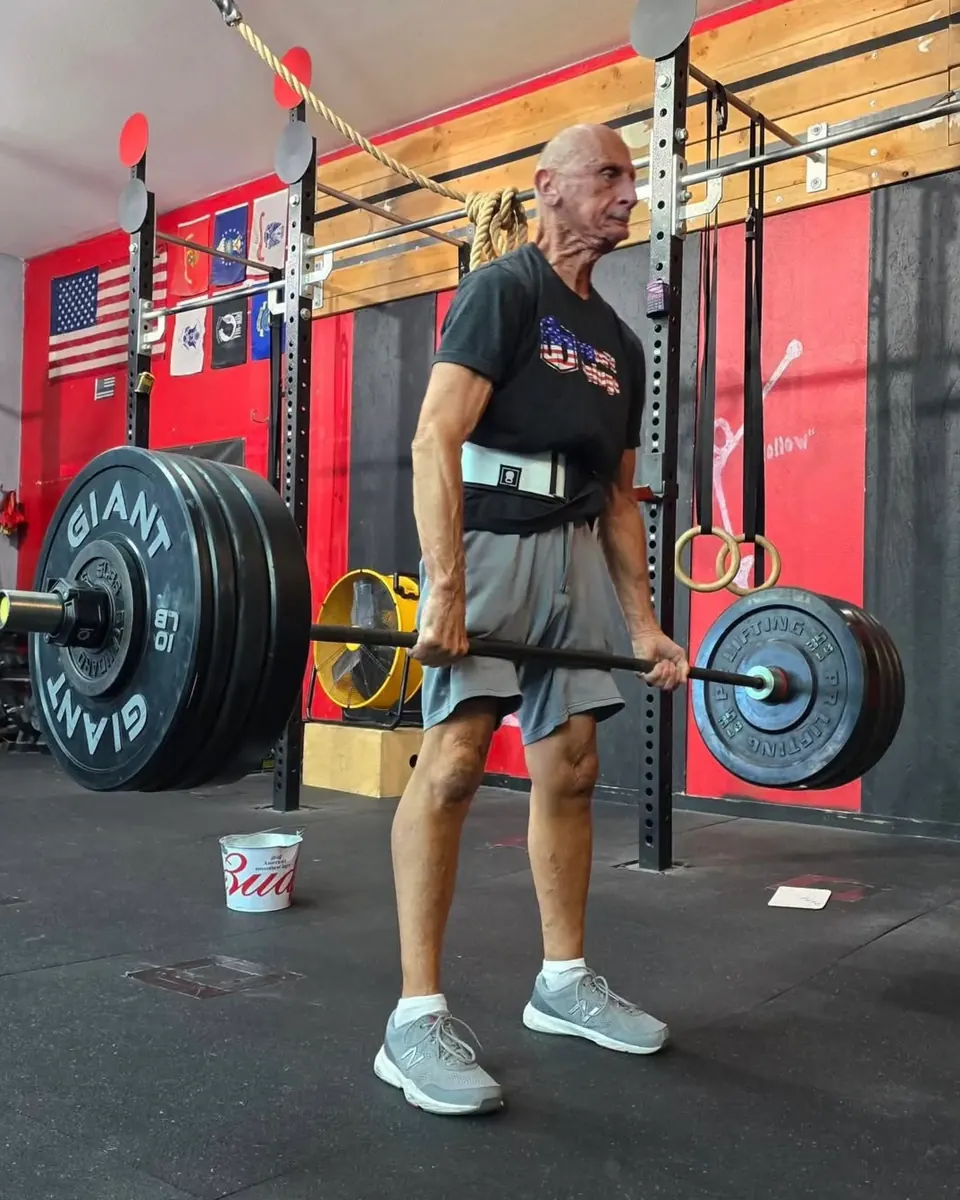 An older Deluge member deadlifting a loaded barbell in the gym.